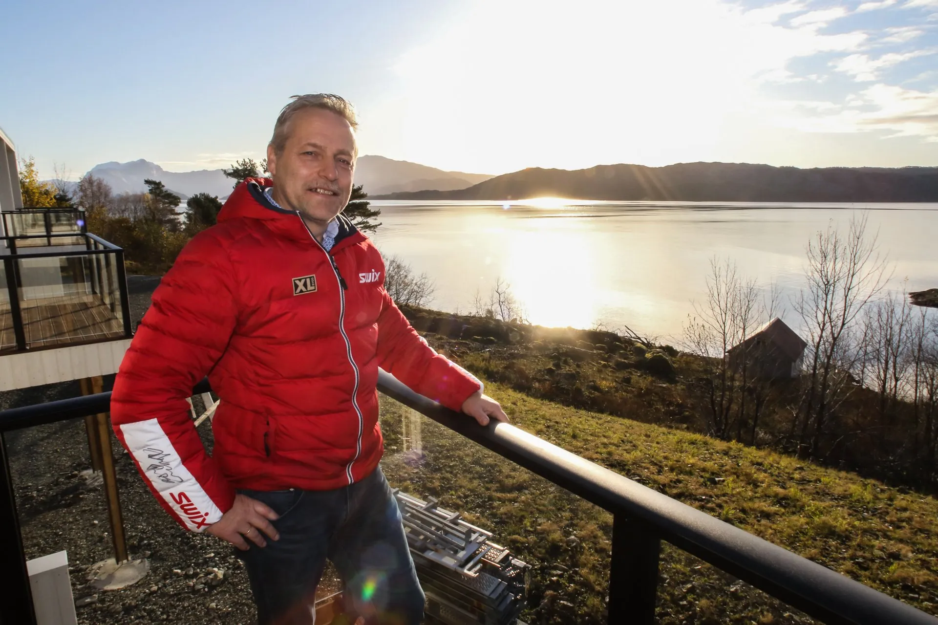 Kjell Sigdestad på ein veranda med fjorden og kveldssola bak seg